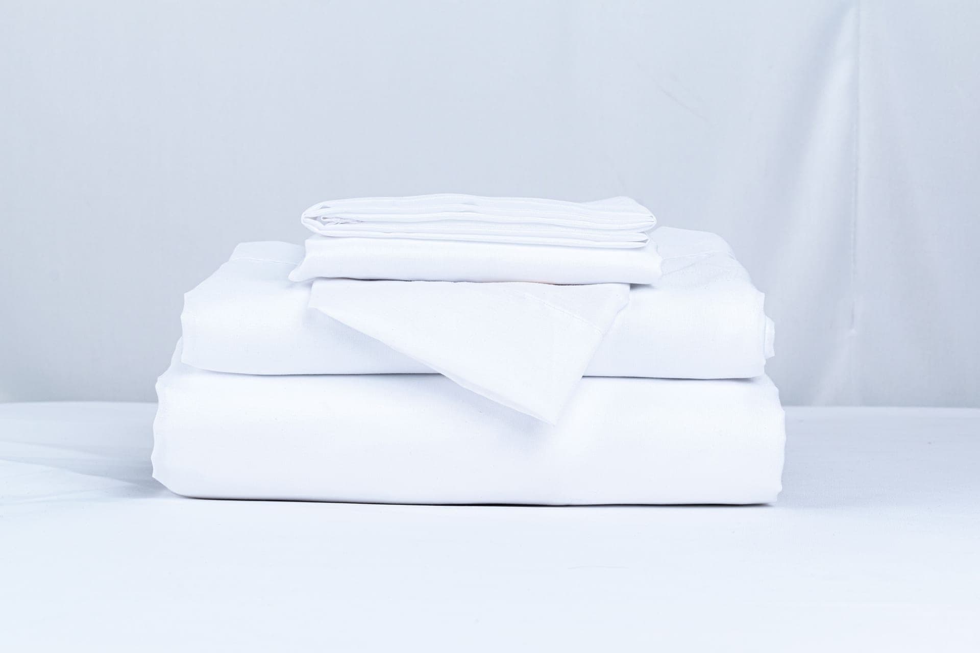 Folded organic cotton and linen bedding beside a green plant sprig