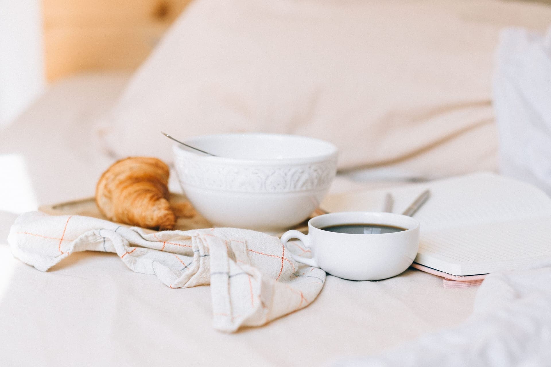 An open notebook and coffee on rumpled linen bedding in morning light
