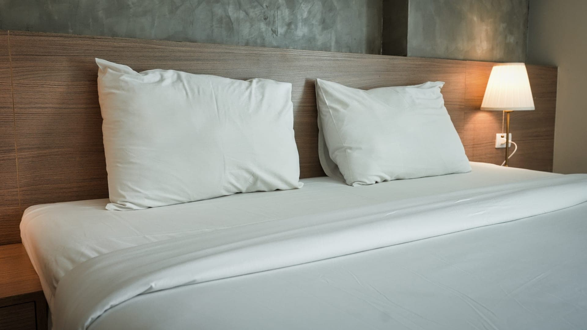 A neatly made bed with a thick mattress in warm morning light